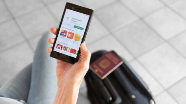 Milan, İtalya - 01 26 2020: Akıllı telefon için Dijital Sağlık Pasaportu uygulaması. Pasaportu ve bagajı olan bir kadın gidiyor..