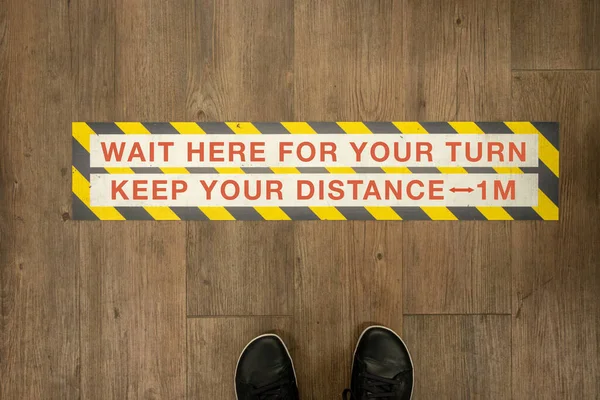 Wait your turn, keep your distance sign on a store floor.