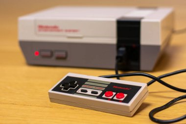 Tahta zemin üzerinde bir Nintendo Eğlence Sistemi Kontrolörü konsola bağlı.