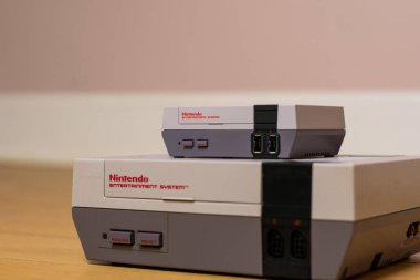 Bir Nintendo Entertainment System Classic Edition on a Top of a Original Nintendo Entertainment System, ahşap zeminde. Orijinal NES ile NES Klasik Sürüm karşılaştırması