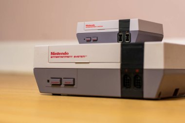 Bir Nintendo Entertainment System Classic Edition on a Top of a Original Nintendo Entertainment System, ahşap zeminde. Orijinal NES ile NES Klasik Sürüm karşılaştırması