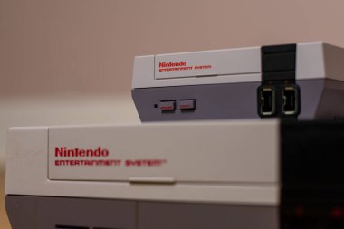 Bir Nintendo Entertainment System Classic Edition on a Top of a Original Nintendo Entertainment System, ahşap zeminde. Orijinal NES ile NES Klasik Sürüm karşılaştırması