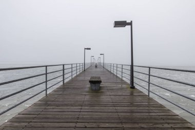 Kasvetli Kış Günü. Uzun bir iskele bulutlu bir kış gününde ağır bir sise dönüşür..