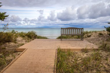 The End. Boardwalk path to an empty park bench overlooking a beautiful lake horizon on the coast of Lake Superior. clipart