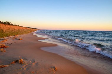 Michigan Gölü kıyıları boyunca uzanan kumsalda altın bir günbatımı dalgalar kıyıya vururken.