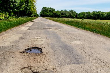 Korkunç Michigan Yolları. İki kırsal şeritli asfalt yolda kocaman bir çukur, çatlamış asfalt ve kaldırımda hiç çizgi yok..