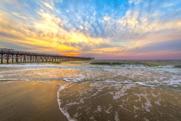 Sunrise over an Atlantic Ocean beach with wooden fishing pier in downtown Myrtle Beach, South Carolina.