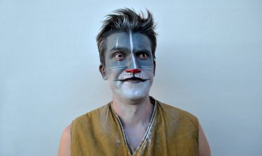 Sarı kolsuz tişörtlü bir adam, gri bir kediyle süslenmiş, yüzünde bir gülümsemeyle şaşırmış, bir kaşını diğerinin üstüne kaldırmış..