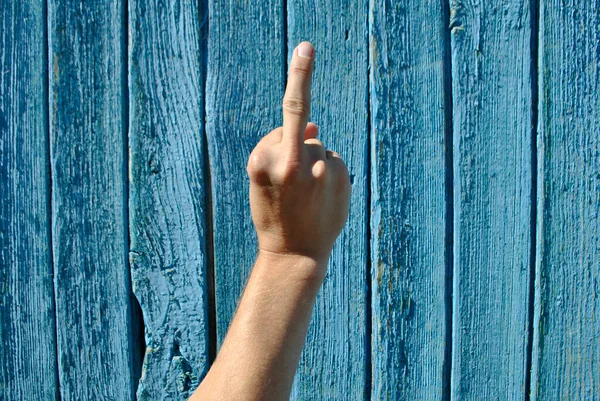 A man\'s hand shows the middle finger on a blue wooden background.