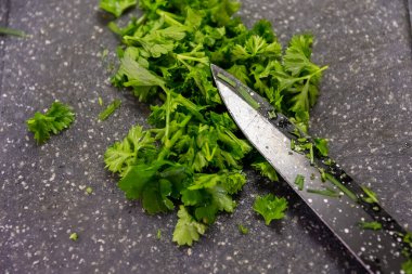 Süslemek için taze maydanoz doğramak ya da otları yakından gören bir salata ve kesme tahtasının üzerinde keskin bir mutfak bıçağı.