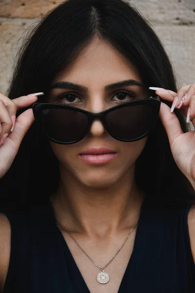 Serious young woman with a thoughtful intense expression lowering her sunglasses to stare at the camera in a close up cropped head and shoulders portrait