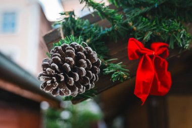 Çok güzel süslenmiş bir tezgahta sergileniyor. Yeşilliğe yaslanmış buzlu bir kozalak ve canlı kırmızı bir fiyonk. Bu şenlikli düzenleme tatil sezonunun ruhunu yansıtıyor..