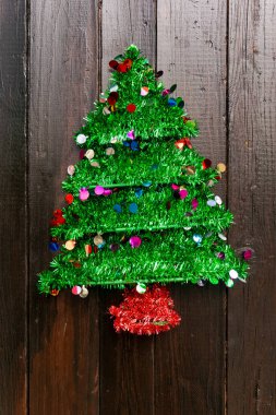 Canlı yeşil bir Noel ağacı renkli konfetilerle süslenir ve kırsal bir ahşap duvara yaslanır. Bu dekorasyon festival sezonuna eğlenceli bir dokunuş katıyor..