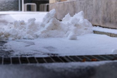 Yumuşak beyaz kar zemini kaplayarak yumuşak tepecikler ve desenler oluşturur. Kentsel ortam serin bir kış gününde sakin bir atmosferi ortaya çıkarıyor. Şehirde bir huzur anı..