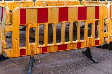 Parlak sarı inşaat bariyerleri hareketli bir caddenin bir bölümünü işaretliyor. Çevredeki binalar ve araçlar bu şehir ortamının canlı atmosferine ekleniyor.