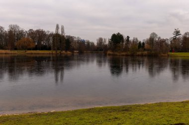 Sakin sular bulutlu gökyüzünü ve etrafındaki ağaçları yansıtıyor ve huzurlu bir manzara yaratıyor. Bereketli yeşil çimenler gölü çerçeveler, derin derin düşüncelere daldırır..