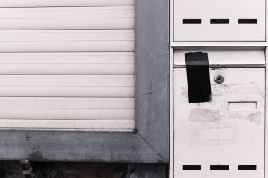 Şehrin sessiz bir köşesinde, eski bir posta kutusu yıpranmış bir kepenk karşısında duruyor. Çatlamış yüzeyi ve solmuş boya işaretleri unutulmuş mektuplar ve bir zamanlar yoğun olan bir bölgedeki bağlantılarını kaybetmiş..