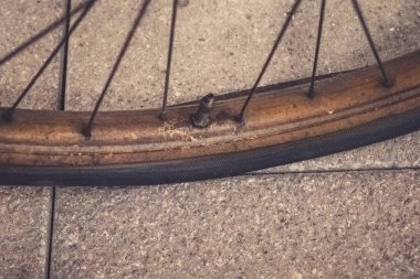 A weathered bicycle tire lies on a textured concrete surface, showcasing its rusty rim and dust accumulation. Gentle sunlight highlights the tire's flaws, hinting at stories of past rides.