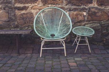 İki eşsiz sandalye, biri büyük, biri küçük, kırsal bir bankın yanında dokulu taş bir duvara karşı dinleniyor. Nane yeşili tonlar ve yumuşak kıvrımlar hoş bir atmosfer yaratır..