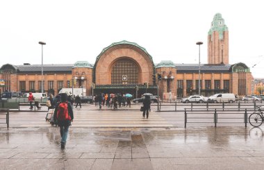Halk, Finlandiya 'daki ünlü Helsinki merkez tren istasyonunun önünde yağmurun altında yürür.