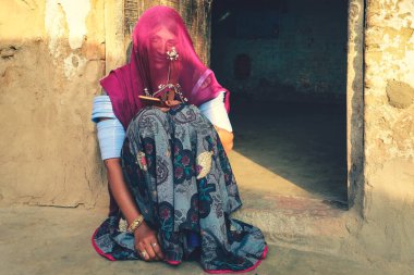 Jaisalmer, Hindistan - 19 Ocak 2020: Hint Rajasthani kadını geleneksel renkli kıyafetler ve mücevherler giyiyor evinin önünde oturuyor