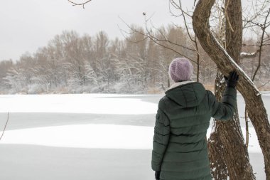 Kız ağacın yanındaki donmuş nehrin yanında tek başına duruyor.