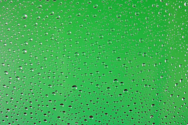 Açık yeşil arka planda cam üzerindeki su damlaları. Soyut