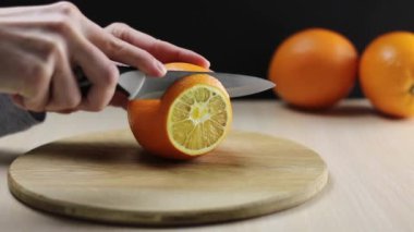 Yuvarlak tahta bir tahtanın üzerindeki kadınlar bıçakla kesiyor olgun bir portakal suyu, sulu bir vitamin. Yavaş çekim. Yakın çekim..