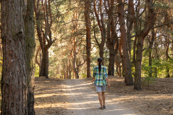 The young woman walks along the road in a pine forest.
