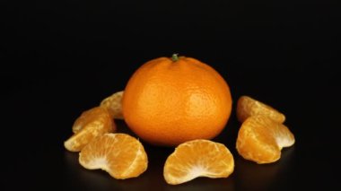 Merkezde koca bir mandalina ve etrafını kesen mandalinalar siyah bir zemin üzerinde dönüyor. Sağlıklı vitaminler yakın plan.