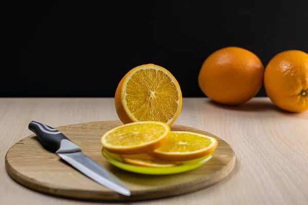 Orange on a wooden round board with sliced slices on a saucer and a knife in the foreground.