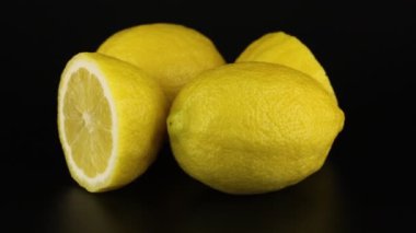 İki tam ve iki yarım limon siyah bir arka planda döner. C vitamini yakın çekim.