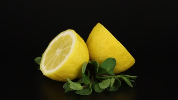 Zwei Hälften Zitronen Und Zweige Minze Rotieren Auf Schwarzem Hintergrund — Stockvideo