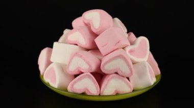 Lokumlar siyah arkaplanda dönen bir fincan tabağında kalp şeklinde pembe ve beyaz renktedir..