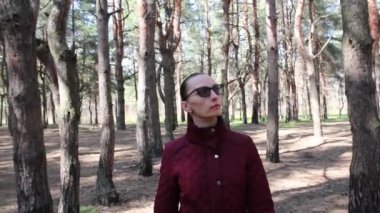 Gözlüklü kadın ormanda yürüyor, etrafa bakıyor, doğanın güzelliğinden zevk alıyor. Ön görünüm.