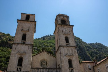Bir dağ manzarası ve yeşil ağaçların arkasında görünen kilise kuleleri. Kotor Montenegro 'daki dağların arkasındaki eski ortaçağ kilisesi
