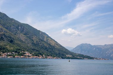Açık bir gökyüzünün arka planında mavi deniz ve yeşil dağlarla kaplı bir manzara. Güneşli şehrin panoramik manzarası. Balkanlar harika bir yaz gününde.