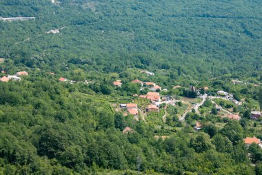 Yeşil dağ manzarası. Kırmızı çatıları olan güneşli şehrin panoramik manzarası. Balkanlar harika bir yaz gününde.