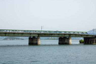 Dağların arka planında güzel göl boyunca uzanan uzun yol köprüsüne bakın. Beton ve demir yapı.