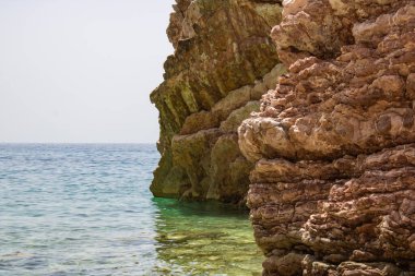 Kayalar güzel suyun üzerinde duruyor. Kayalık sahil kıyısı. Denizin arka planında büyük bir taş var. Büyük taşlar grubu.