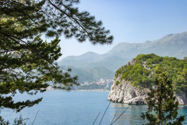 Açık bir gökyüzünün arka planında mavi deniz ve yeşil dağlarla kaplı bir manzara. Güneşli şehrin panoramik manzarası. Balkanlar harika bir yaz gününde.
