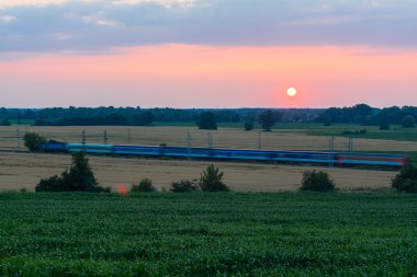 Tren, tren arabaları ile günbatımı kırsal kesimde izler.