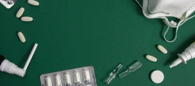 Tıbbi ekipmanlar, haplar, boğaz spreyi, termometre ve koruyucu maske, yeşil bir arka planda yatıyor. Yakın çekim.