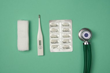 Tıbbi ekipmanlar arka arkaya dizilmiş: şırınga, termometre, paketteki haplar, bandaj, stetoskop. Yakın çekim.