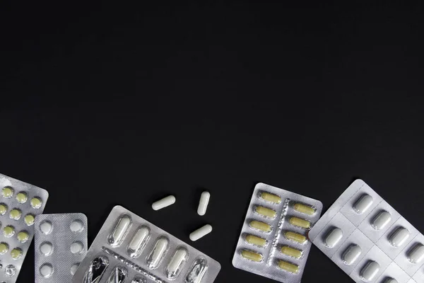 Tabletler ve kapsüller bir pakette, şırıngalar siyah arka planda yatıyor. Yazı için çerçeve.