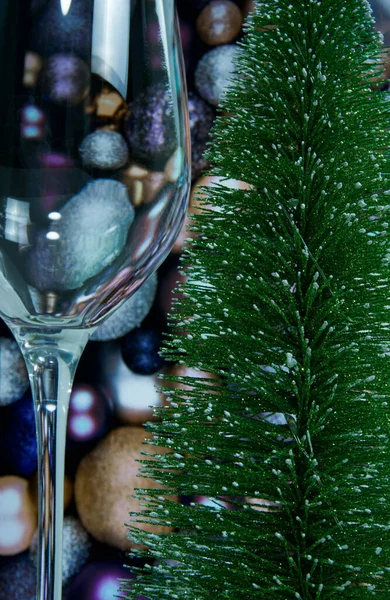 Yapay bir Noel ağacının yanında duran boş bir şarap kadehinin yakın plan fotoğrafı. Altın ve mor Noel toplarının arka planında.