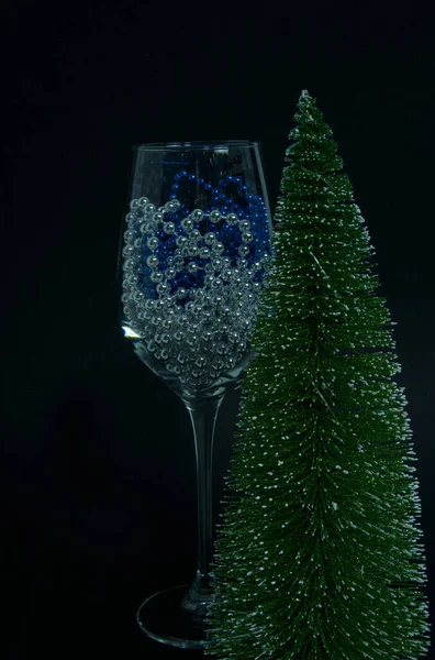 Siyah arka planda bir şarap kadehi bir Noel ağacının yanında duruyor. Cam mavi ve gümüş Noel süslemeleri içeriyor..