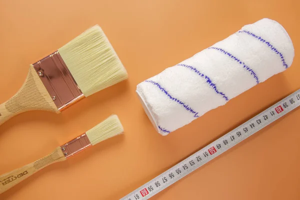 two construction brushes of different widths, a roller and a construction tape lie on an orange background. photo taken close-up from above
