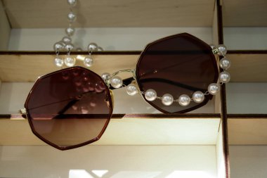 sunglasses close-up, lie on a shelf in a shop window. the glasses are adorned with a pearl glasses chain. filmed in sunlight