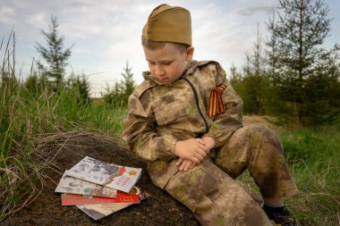 Askeri üniformalı bir çocuk Büyük Vatanseverlik Savaşı kahramanlarının isimlerinin olduğu bir kitaba bakıyor. Zafer Günü.